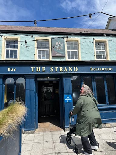Customer with rented rollator outside The Strand bar and restaurant in Dublin on a sunny day with festive bunting overhead